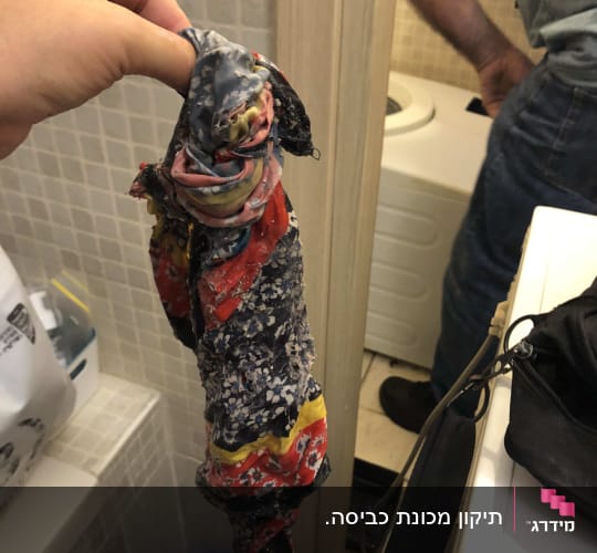 יד מחזיקה חפץ צבעוני ליד מכונת כביסה